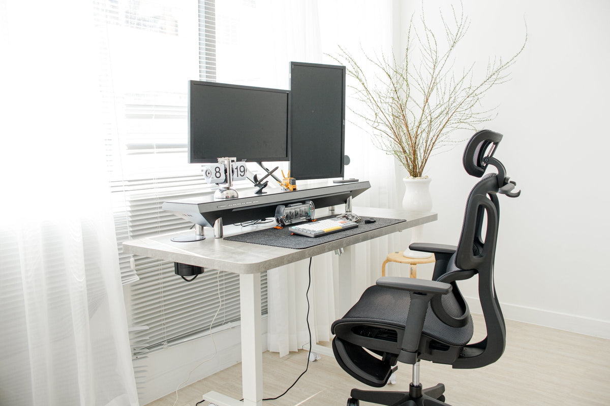 White standing desk with dual monitors, a desk shelf and an ergonomic black mesh chair