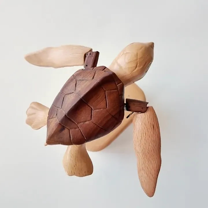 Sea turtle automaton from above, dark shell and four pale flippers against a plain wall.