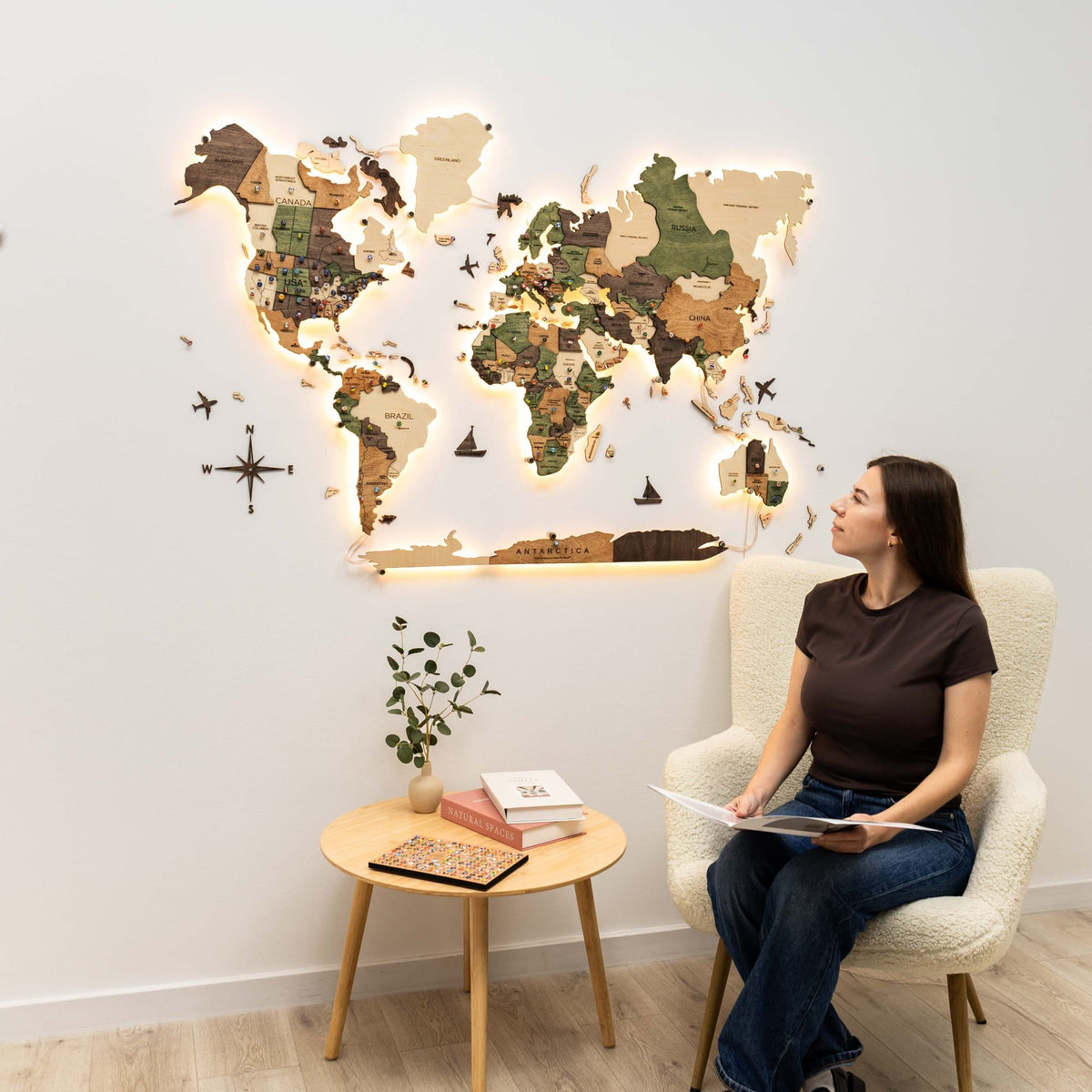 A person sitting in a chair beside the lit wooden world map, a side table and plant in the room