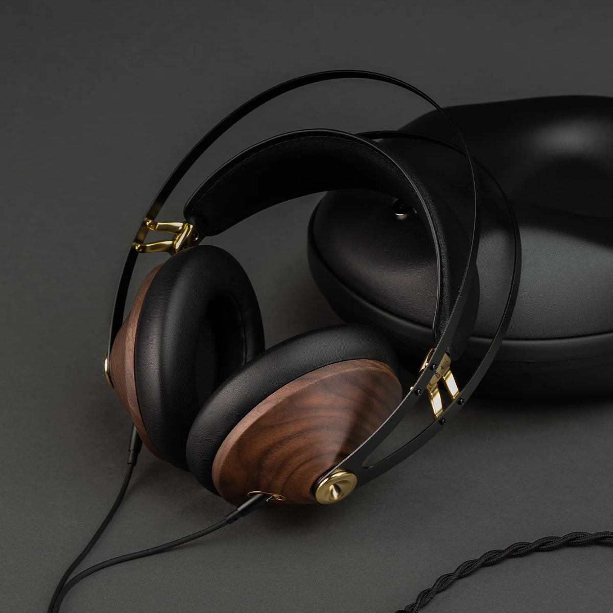 Headphones resting on a dark surface beside their hard case