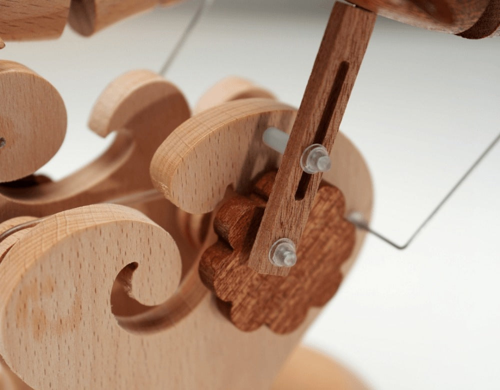 Close up behind the carved waves: a slotted wooden arm and metal pins that lift the dolphins.