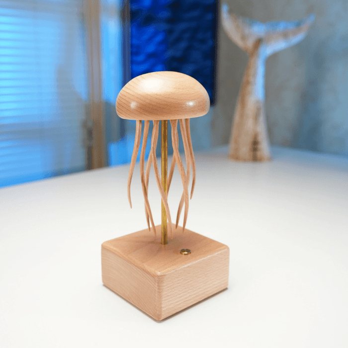 Jellyfish automaton on a white table in a softly lit blue room, a pale whale tail sculpture behind.