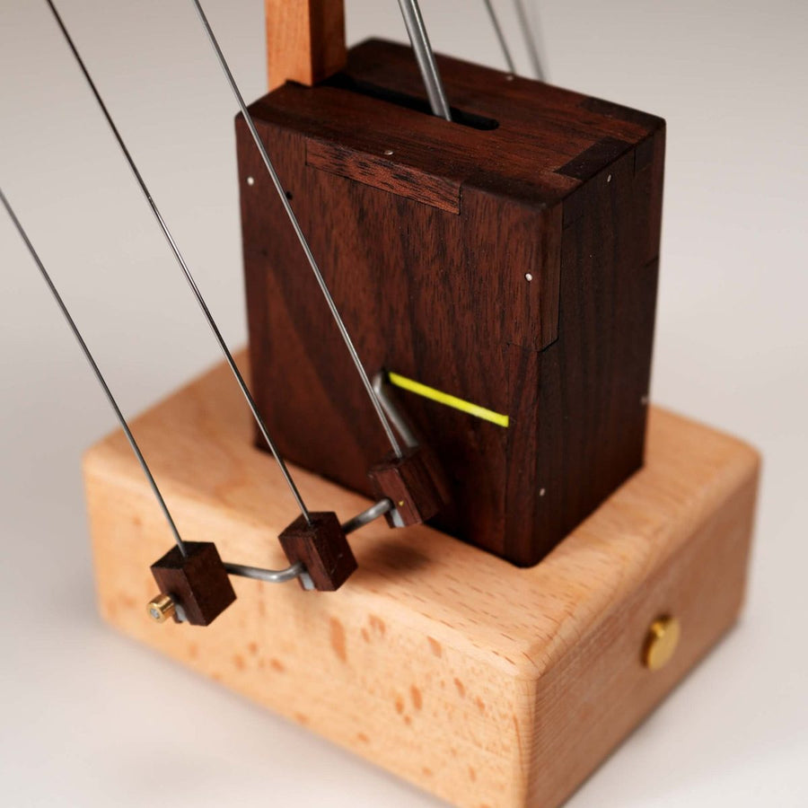Internal gear base: a closed light wood box with a small brass button, the dark tower and wires rising from it.