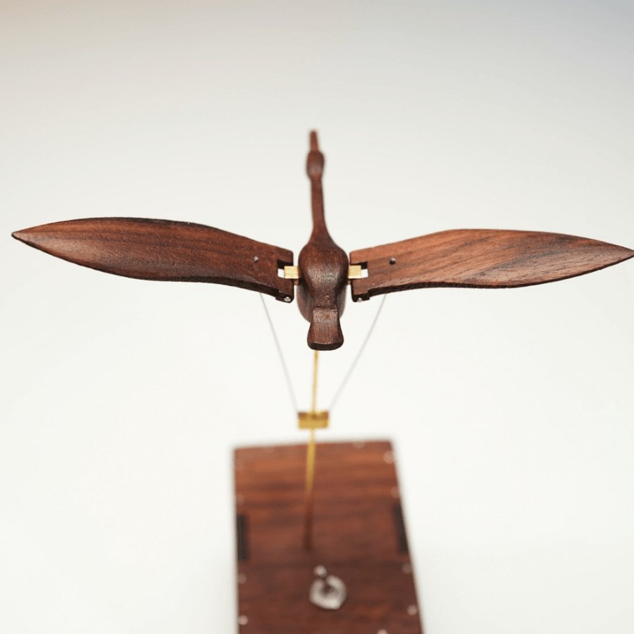 Walnut swan from the front with its wings open above the box on a white table.