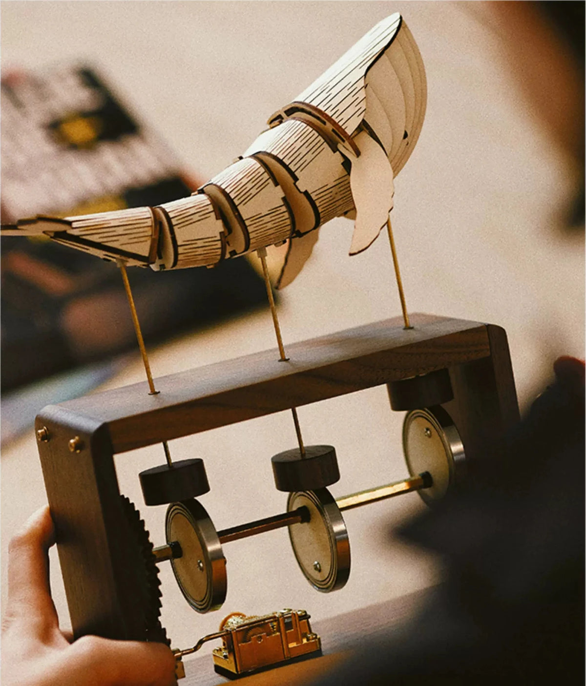 Hands hold a walnut music box with a pale jointed whale on brass rods, three cams and the music box movement in view.