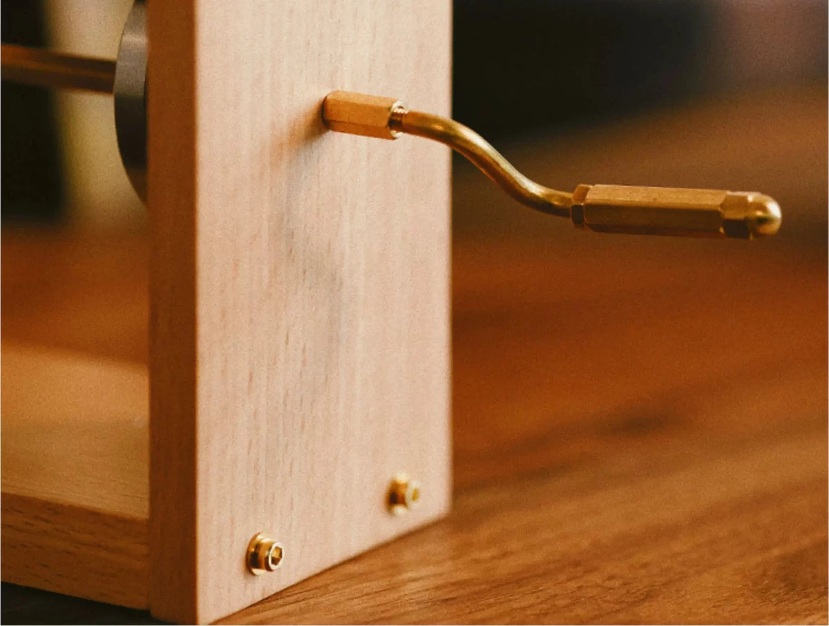 The brass crank on the side of the beech frame, close up, on a wooden table.