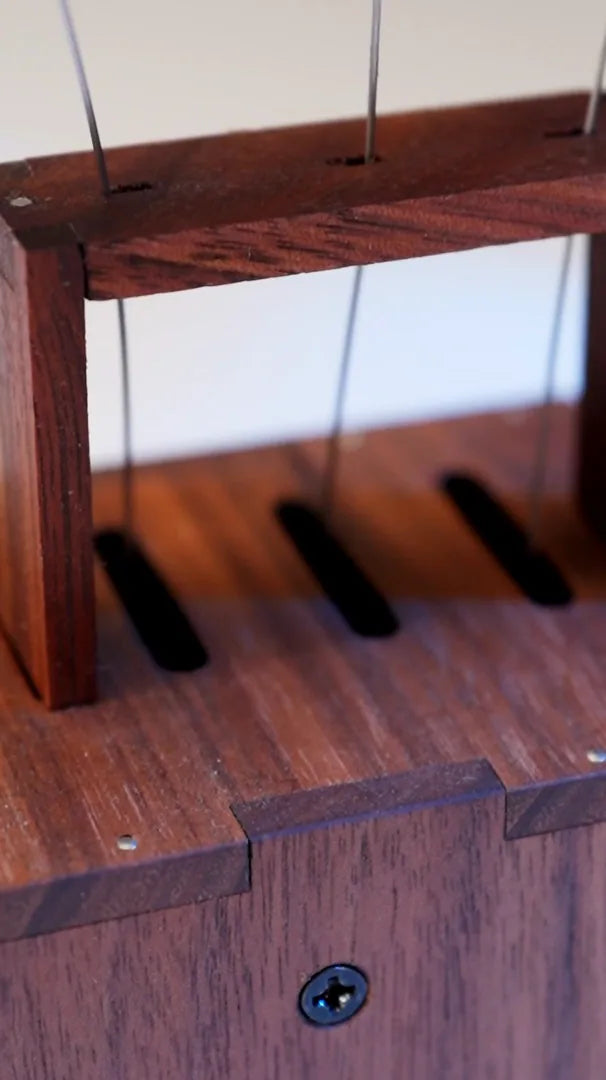 dark wood grain and a finger-joint corner on the box top, black screw and the three long wire slots in focus.