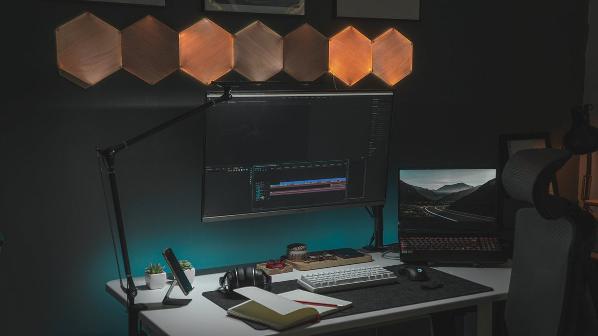 Dark desk under wood hexagon lights with a monitor and laptop