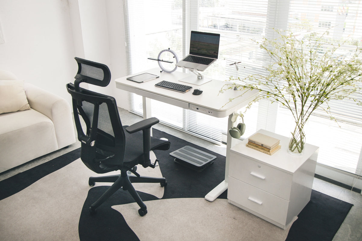 Bright corner office with a white standing desk, mesh chair, drawer cabinet and green headphones