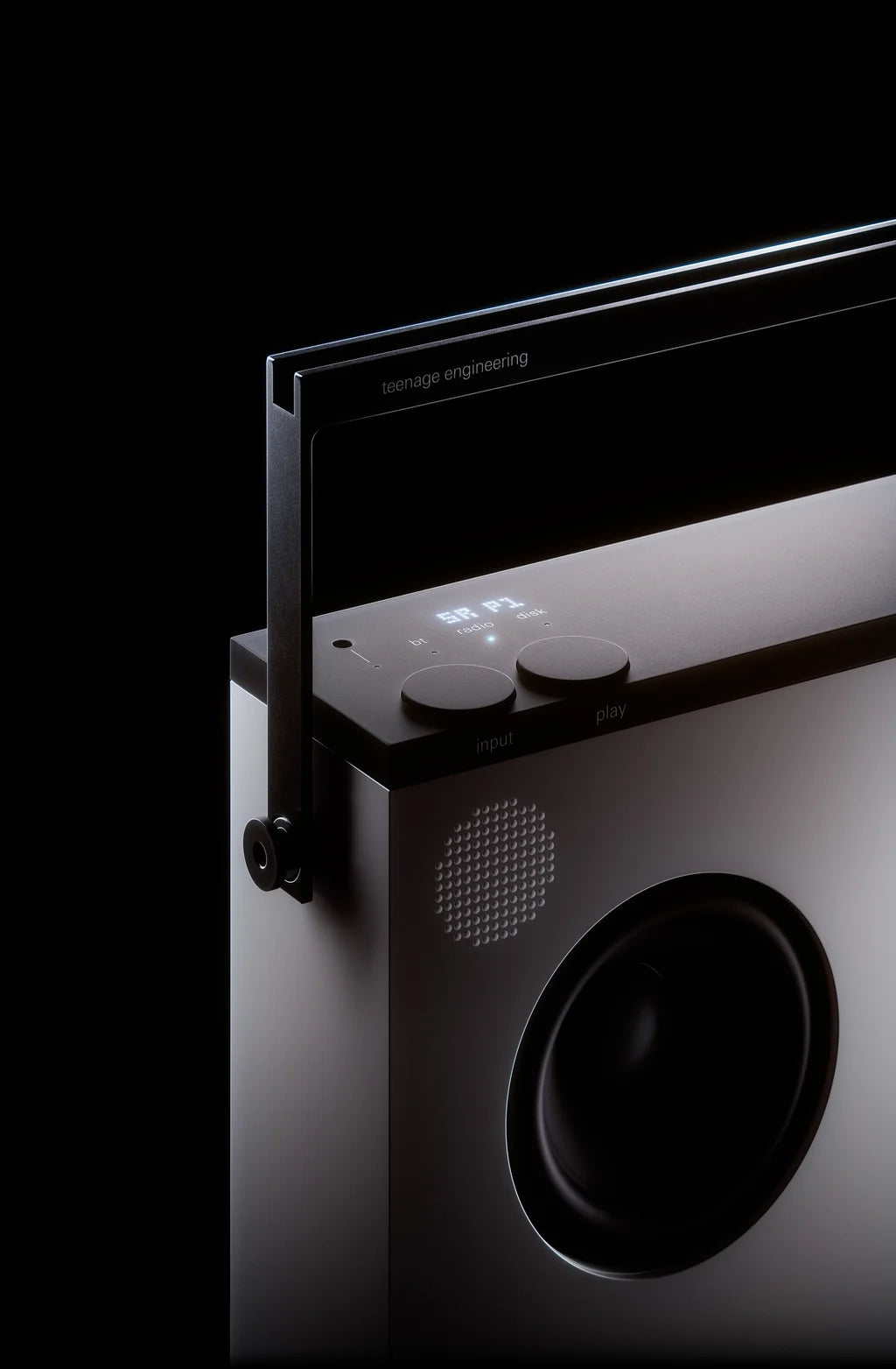 Close-up of the OB-4 top handle, two knobs and one round woofer on a dark backdrop