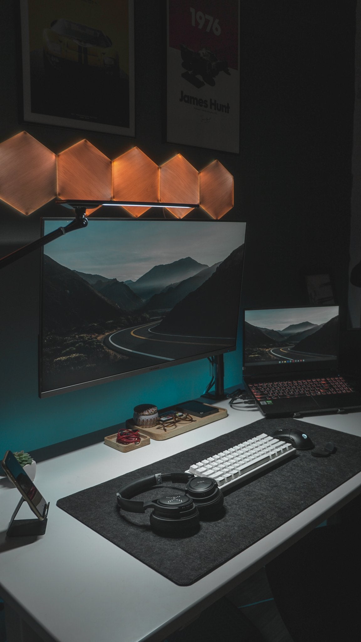 Vertical view of a dark desk with hexagon lights, racing posters and a white keyboard