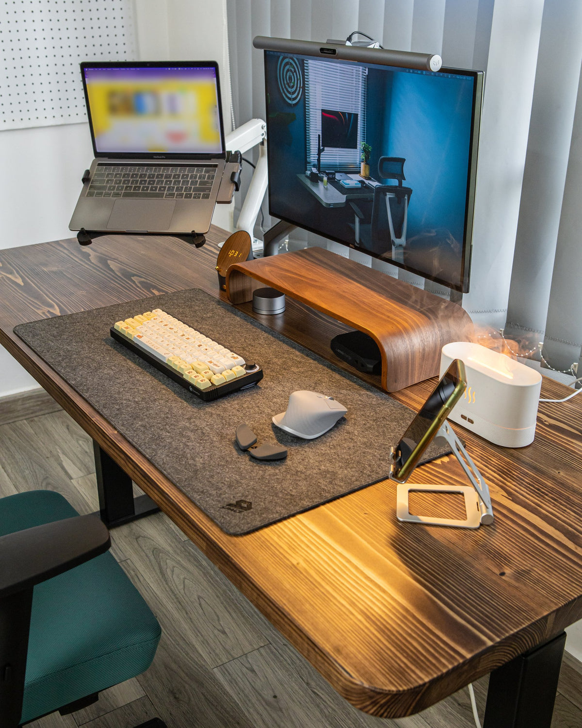 Bright desk setup with a laptop on a stand, monitor with light bar, wooden riser, felt mat and ergonomic mouse