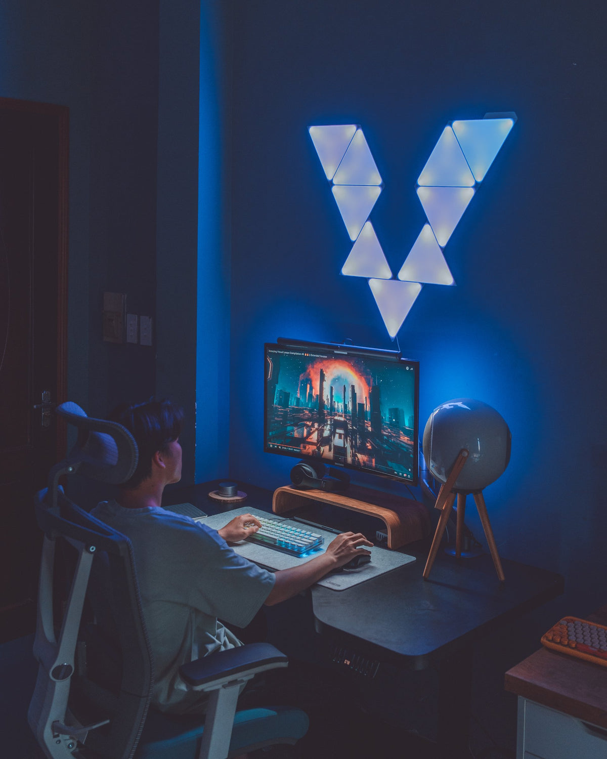Back view of a person at a dark desk under a glowing blue triangle light panel