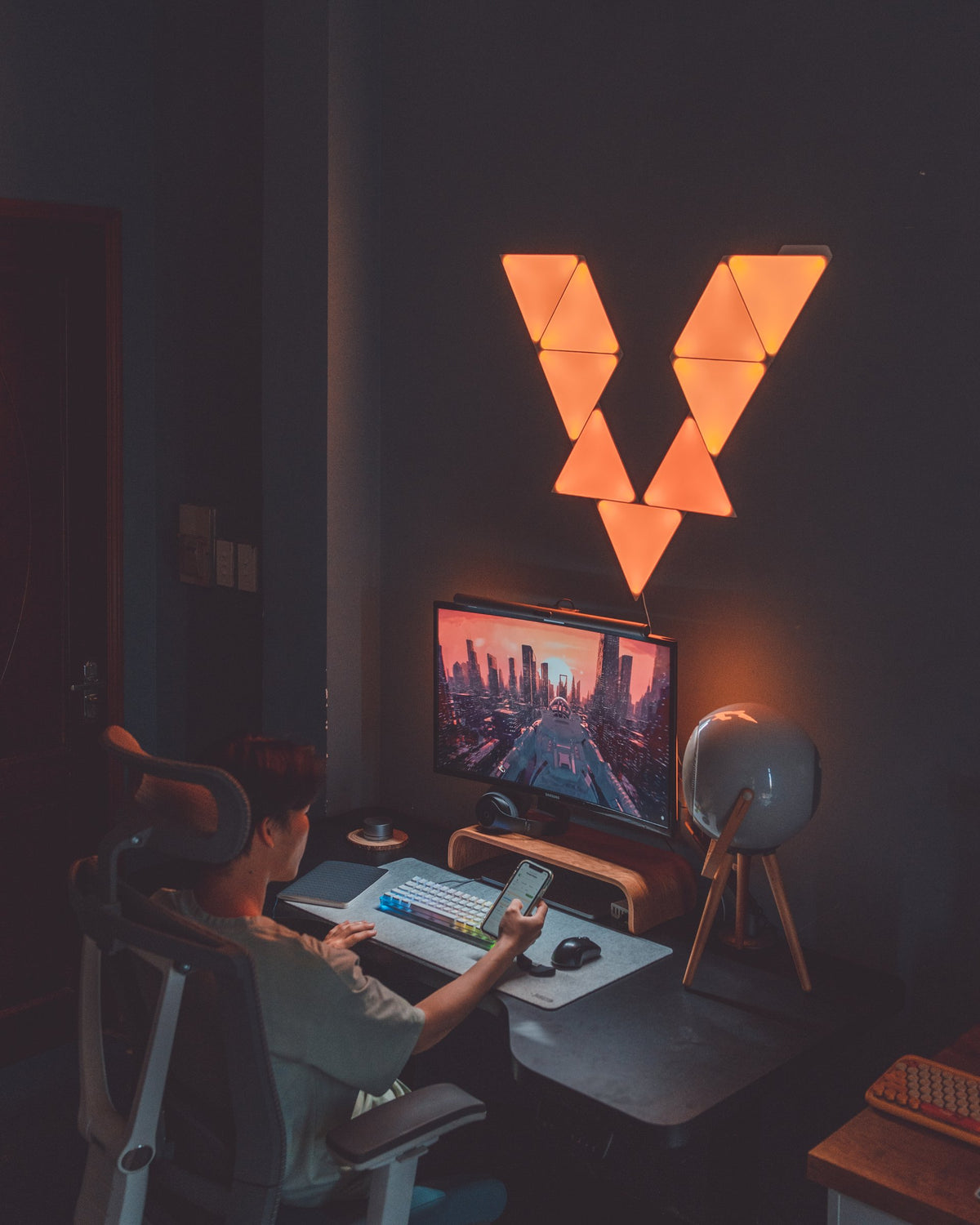 Back view of a person checking a phone at a desk lit by orange triangle light panels
