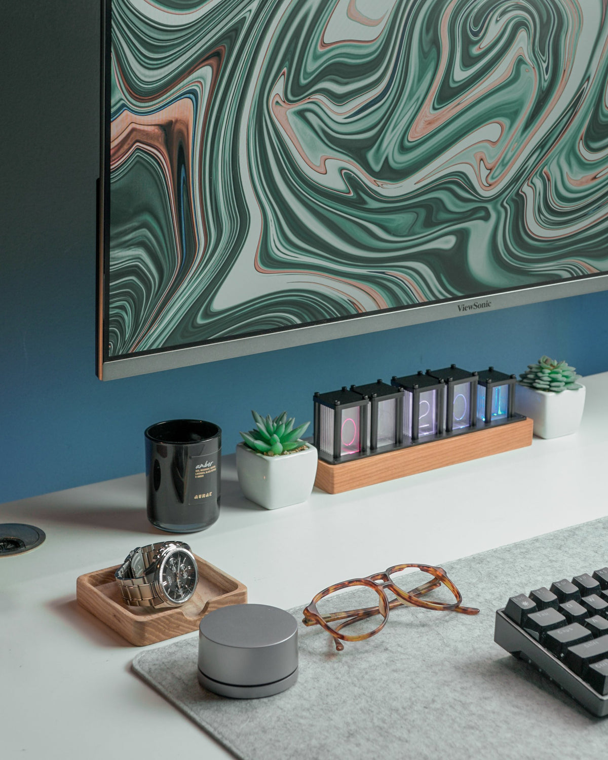 Watch, glasses and small speaker on a white desk under a green marble screen