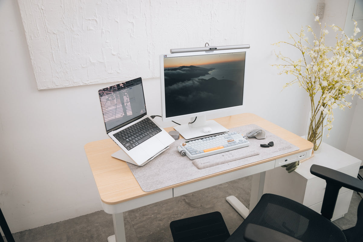Light oak standing desk with a white monitor, laptop stand and flowers