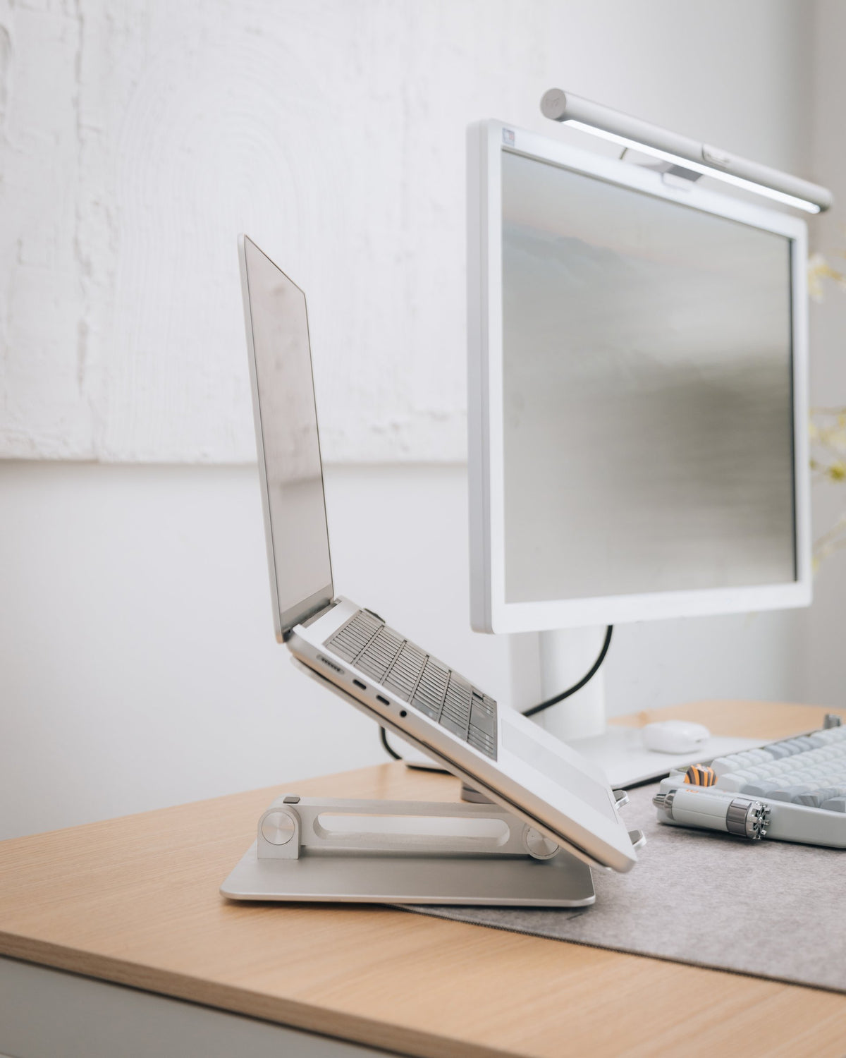 Laptop on a tilted aluminum stand next to a white monitor with a light bar