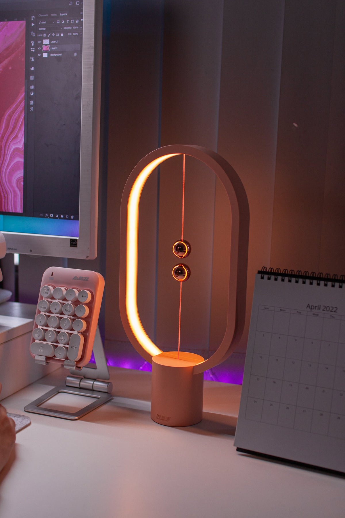 Pink balance lamp and pink numpad beside a monitor on a white desk