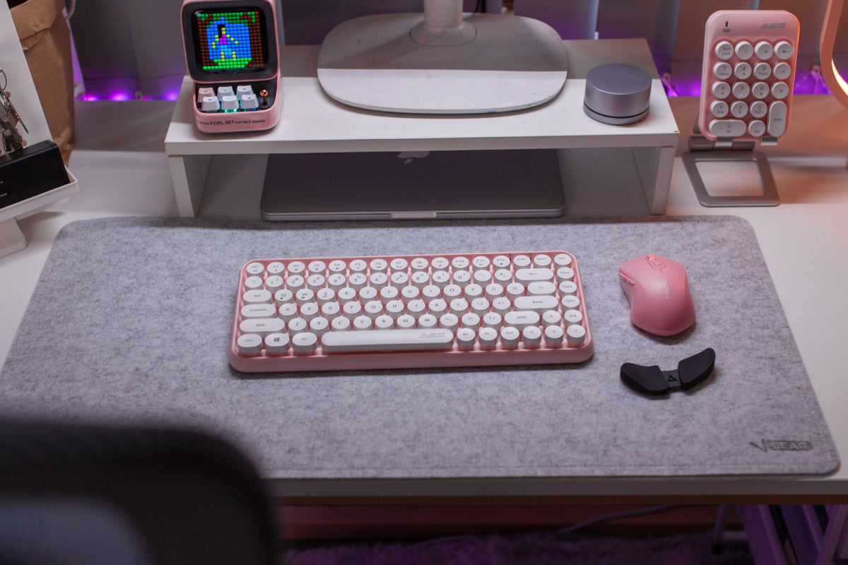 Pastel pink keyboard, mouse and pixel display on a white desk with a monitor shelf
