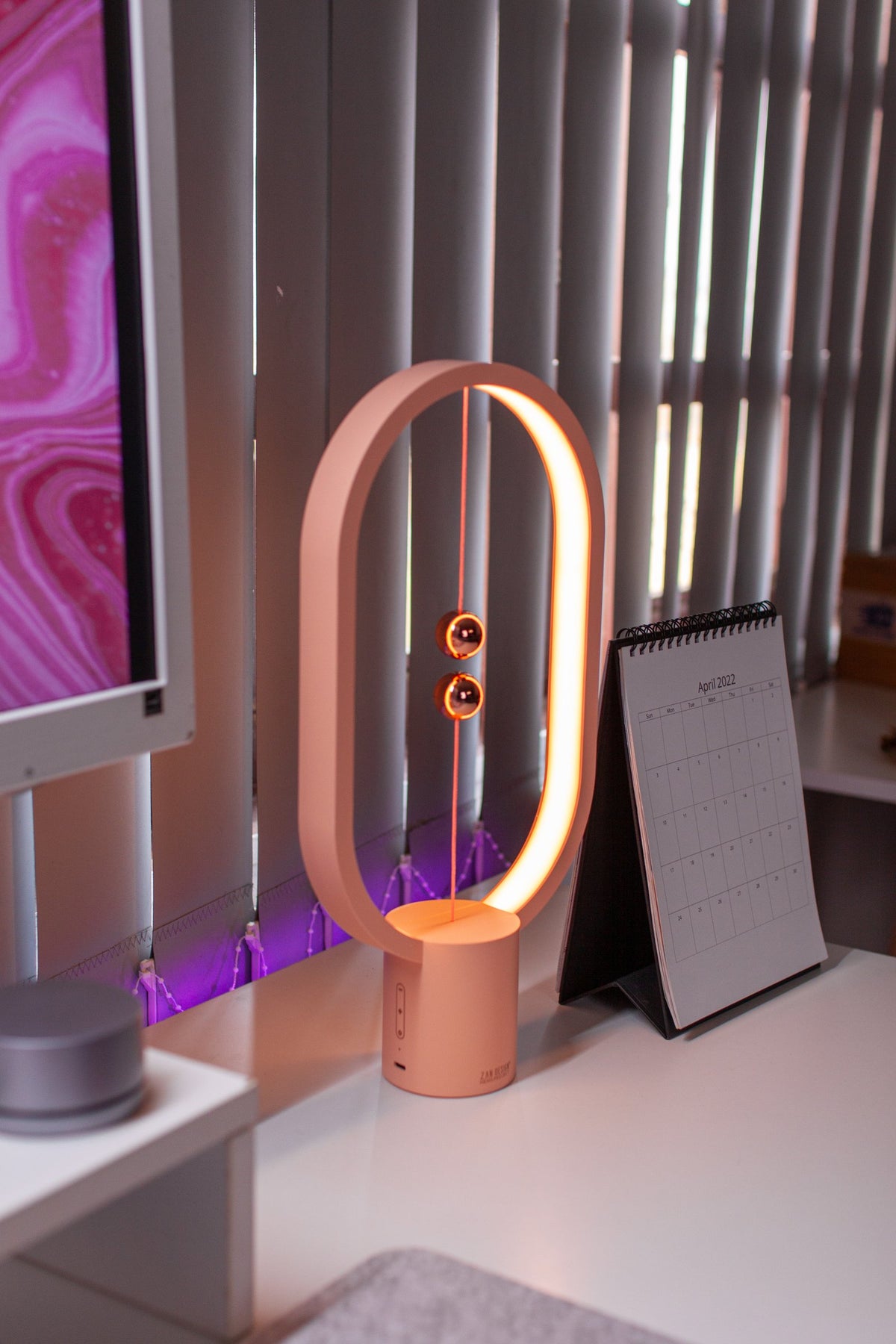 Pink balance lamp next to a desk calendar on a white desk
