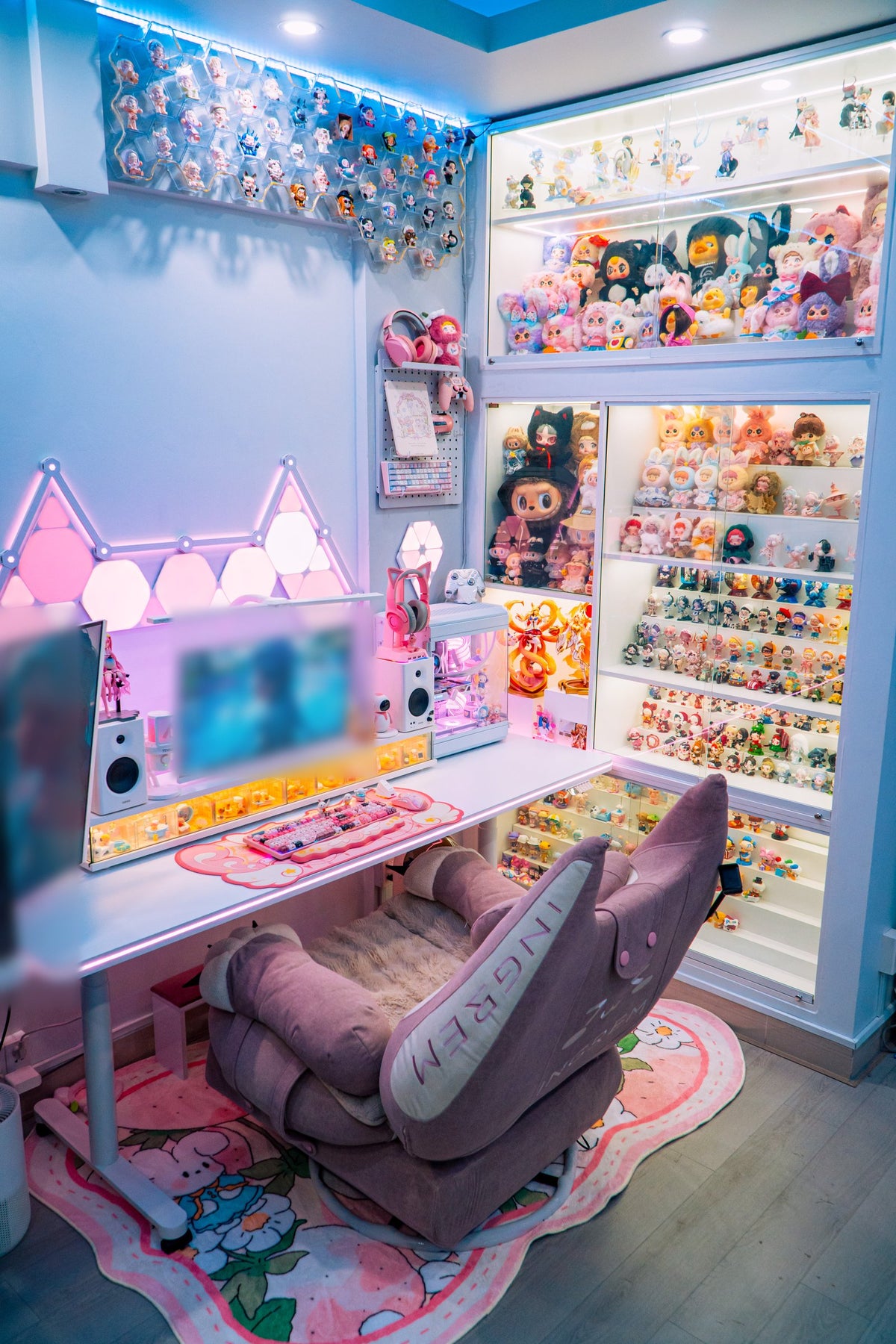 Corner room with display cases of collectible toys, a desk with pink lights and a pink plush recliner