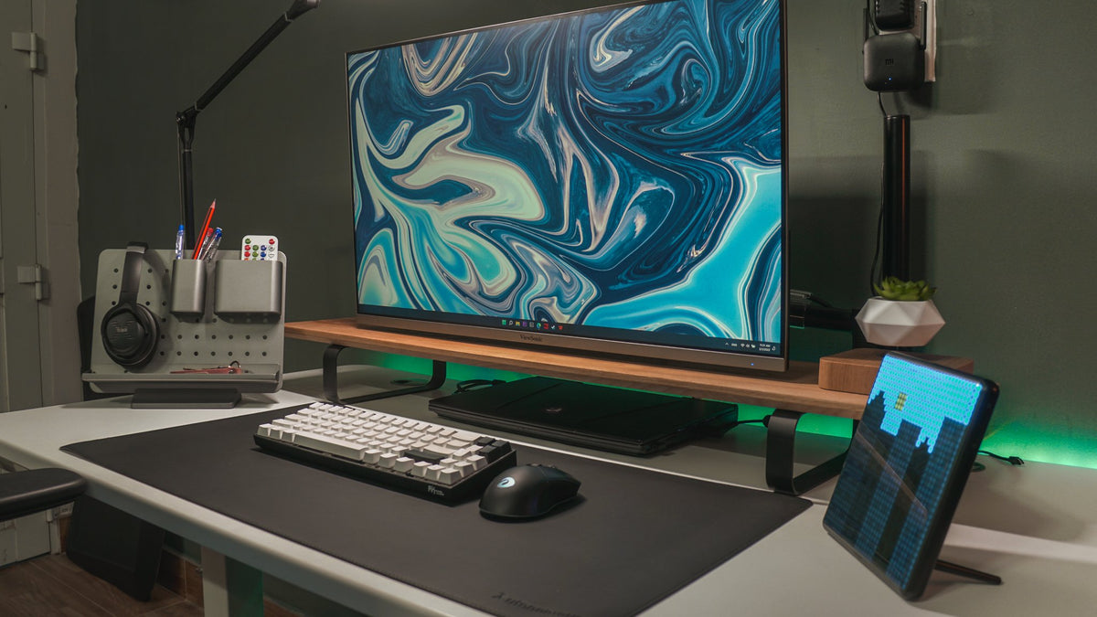 Desk with a blue marble wallpaper monitor, headphones on a pegboard and a pixel display