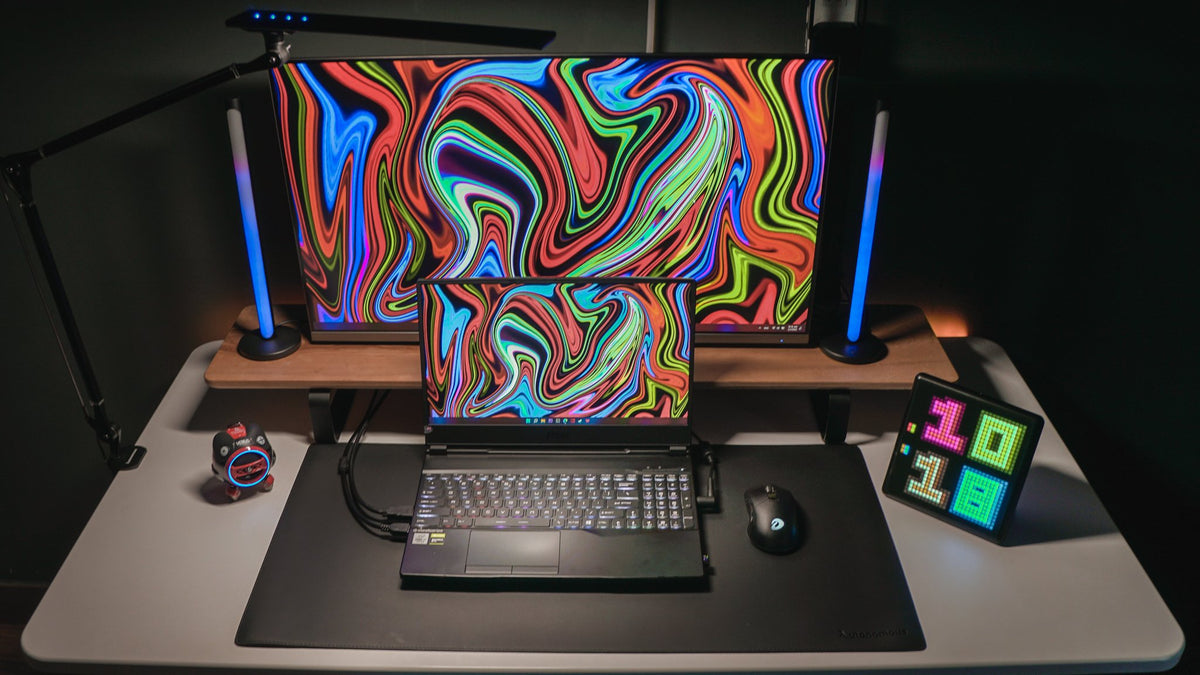 Dark gaming desk with a laptop, monitor, RGB light bars and pixel display