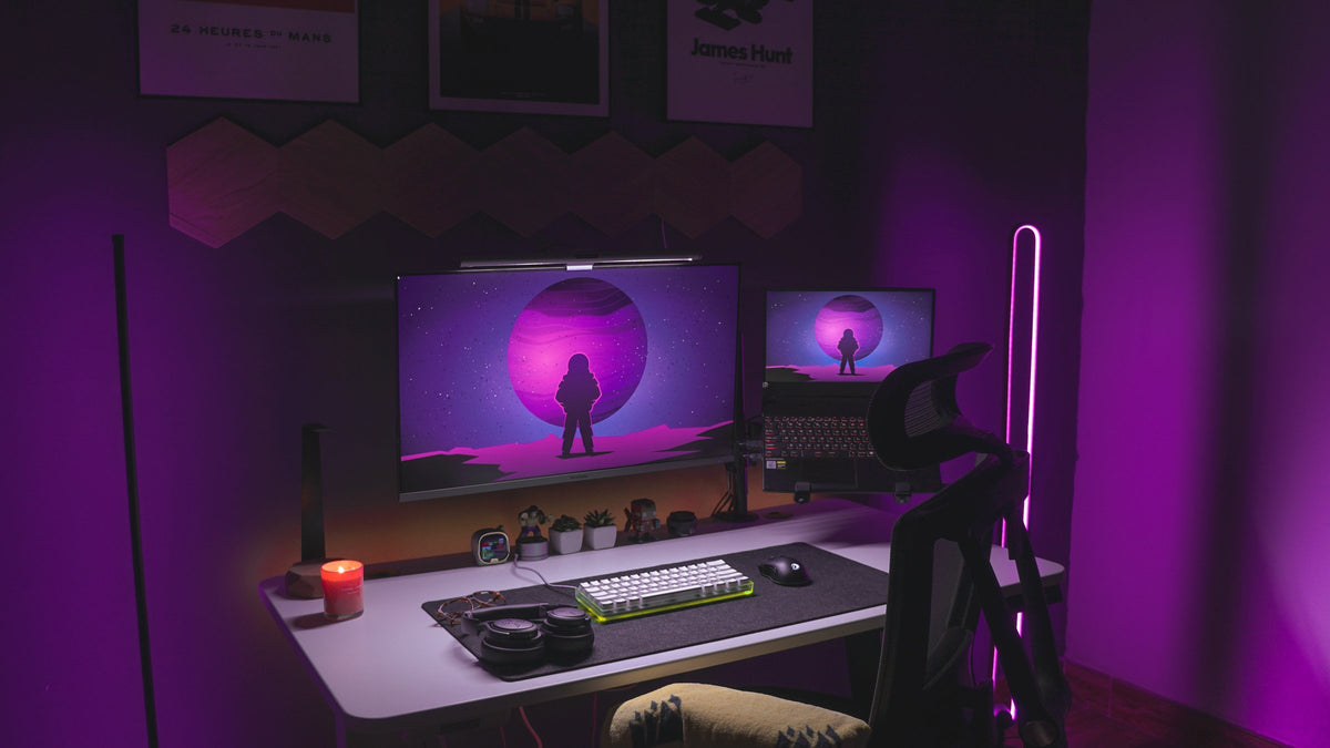 Dark purple room with a white desk, dual monitors, floor lamps and a mesh chair