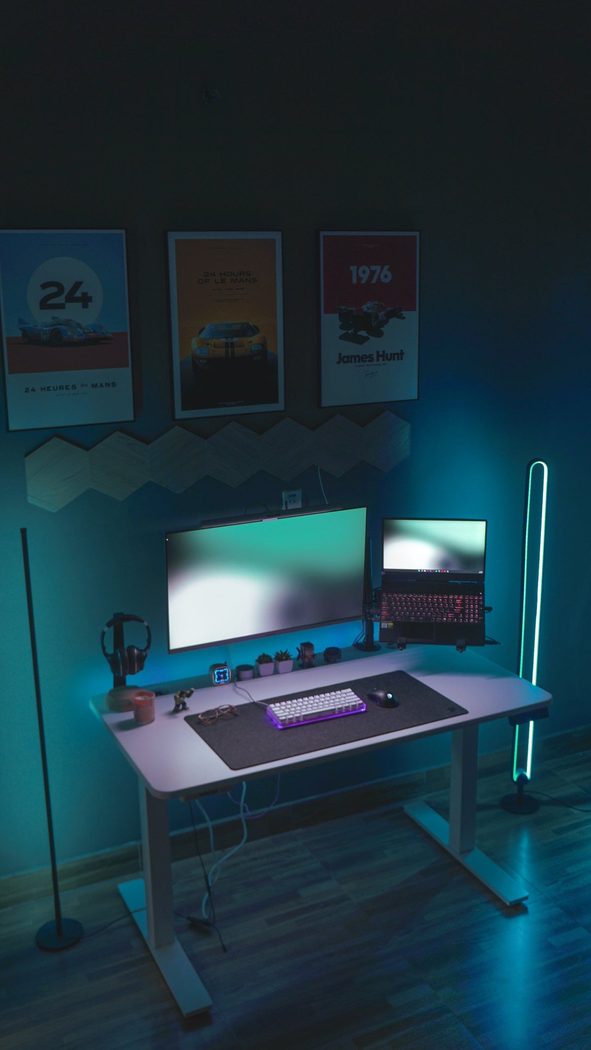 Teal-lit white standing desk with a monitor, laptop and racing posters above