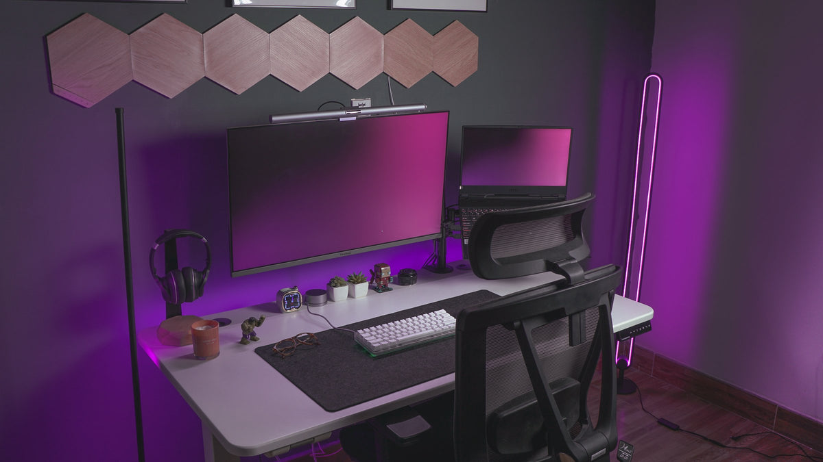 Purple-lit gaming desk with a wide monitor, floor lamps and wood hexagon wall panels