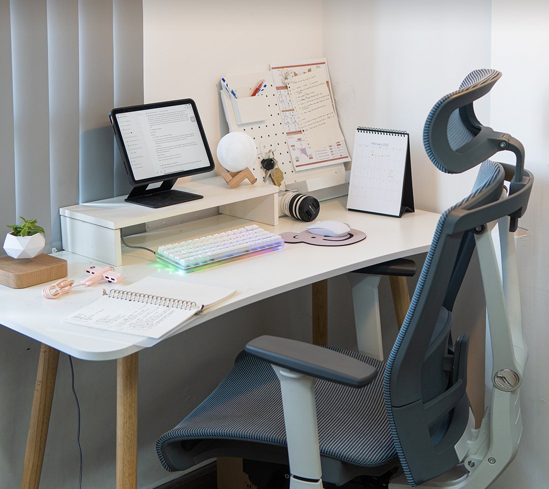 White study desk with a monitor shelf, backlit keyboard, notebook and mesh chair