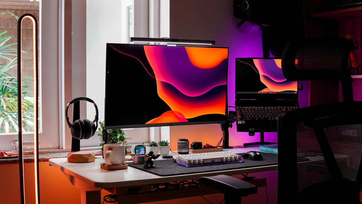 White desk with an orange and purple wallpaper on a monitor and laptop by a window