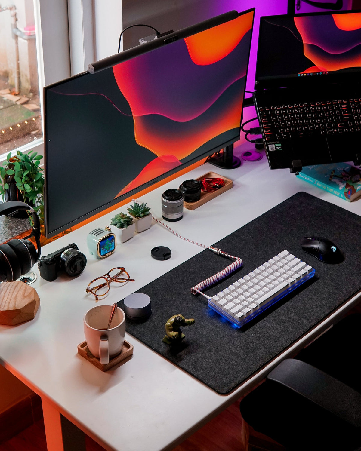 Angled view of a white desk with a dark desk mat, mechanical keyboard and accessories