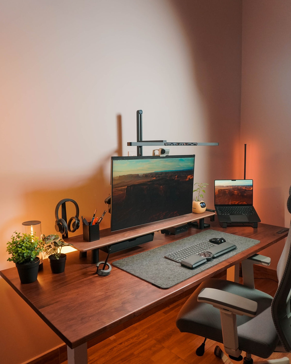 Corner of a walnut desk with plants, headphone stand, monitor shelf and a felt mat