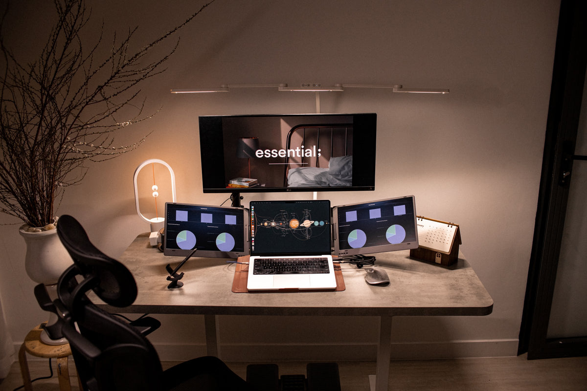 Concrete-top standing desk with three screens, a balance lamp and a mesh chair