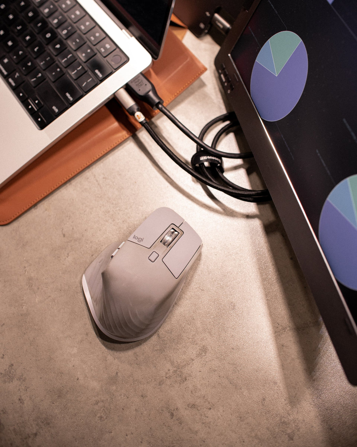 Gray ergonomic mouse on a concrete desk beside a portable monitor