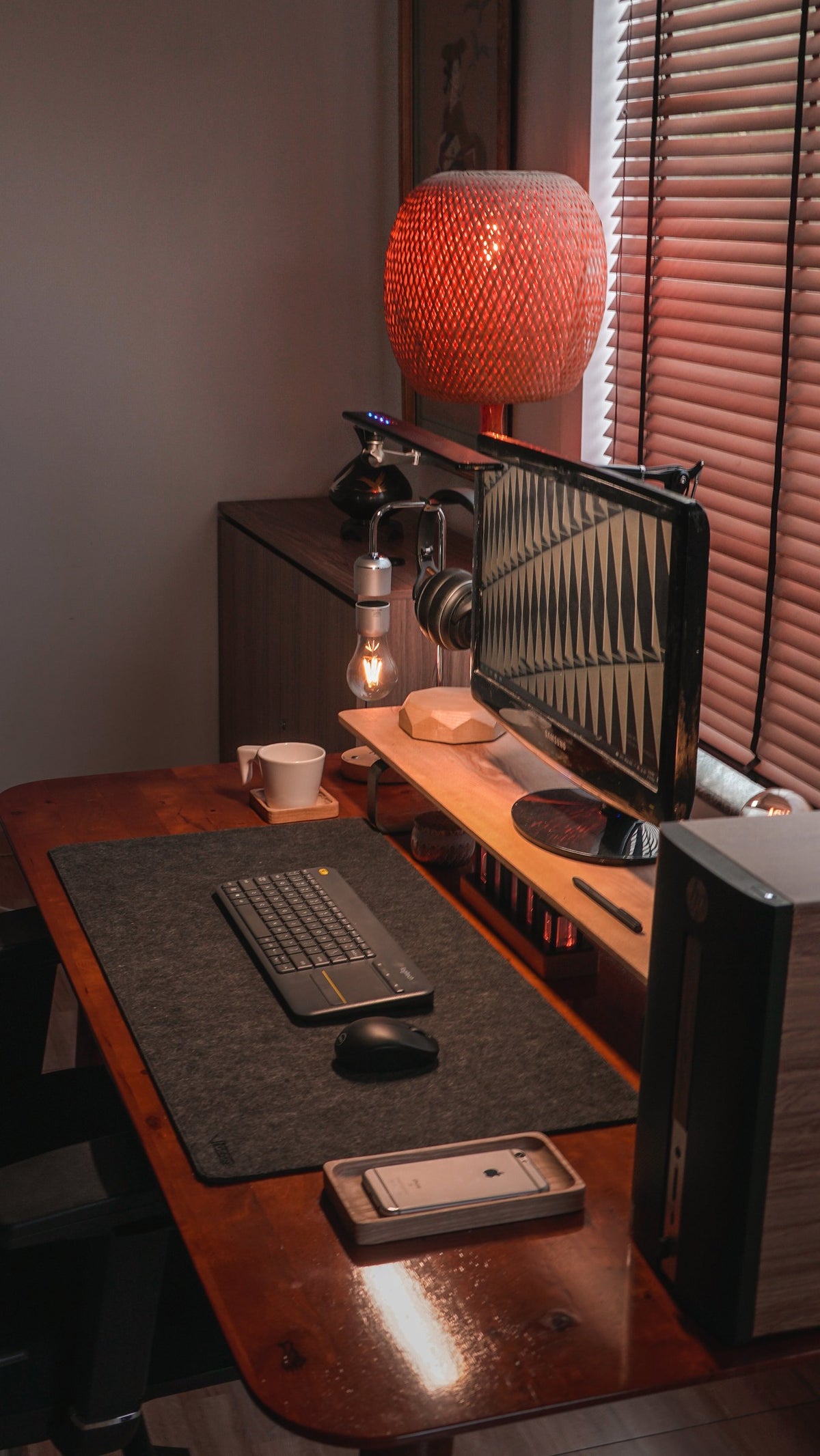 Warm desk corner with a monitor, lamp and keyboard on a dark felt mat