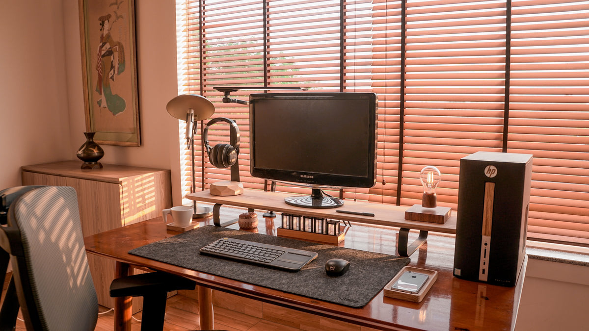 Warm room with a walnut desk, monitor riser shelf, desktop tower and mesh chair by blinds