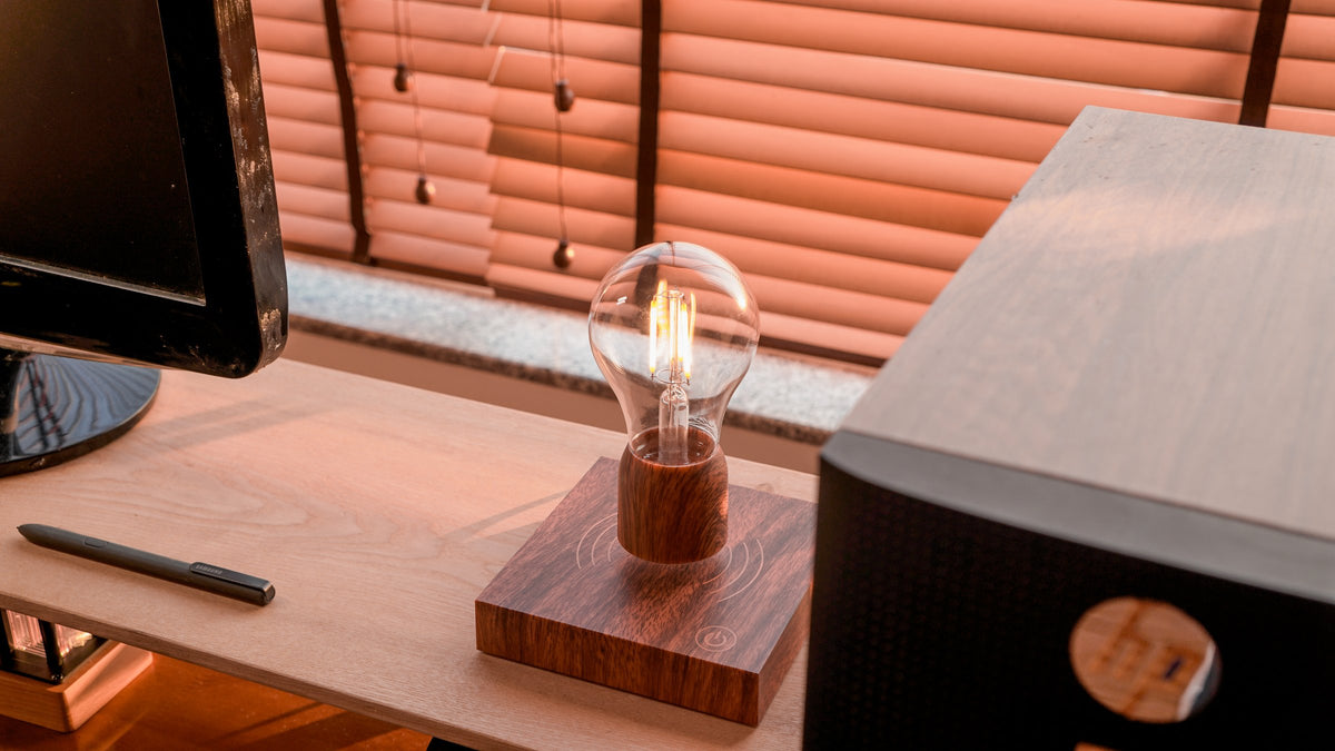 Levitating bulb lamp on a wood desk beside a speaker in warm window light