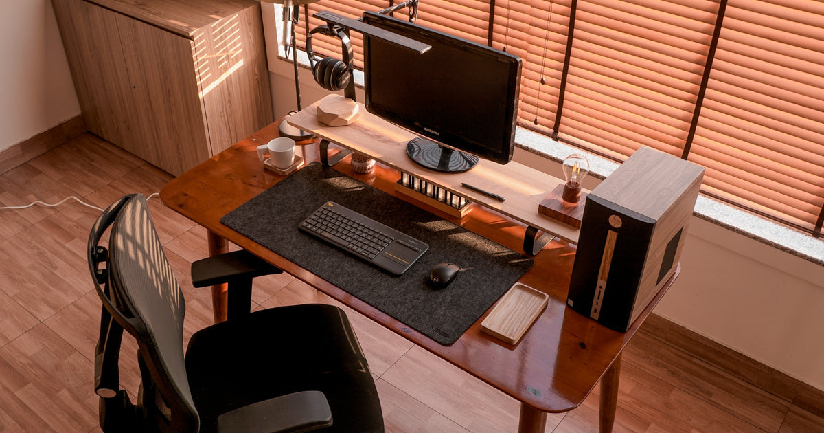 Angled view of a walnut desk with a dark felt mat, keyboard and desktop tower