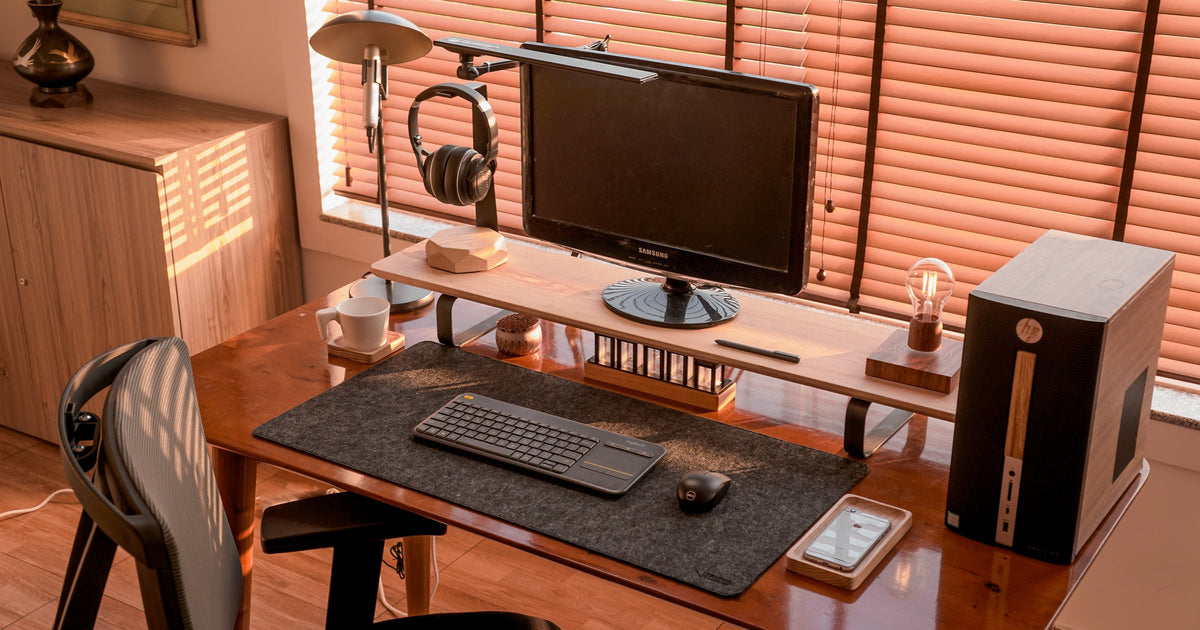 Walnut desk by sunlit orange blinds with a monitor riser, keyboard, desktop tower and mesh chair