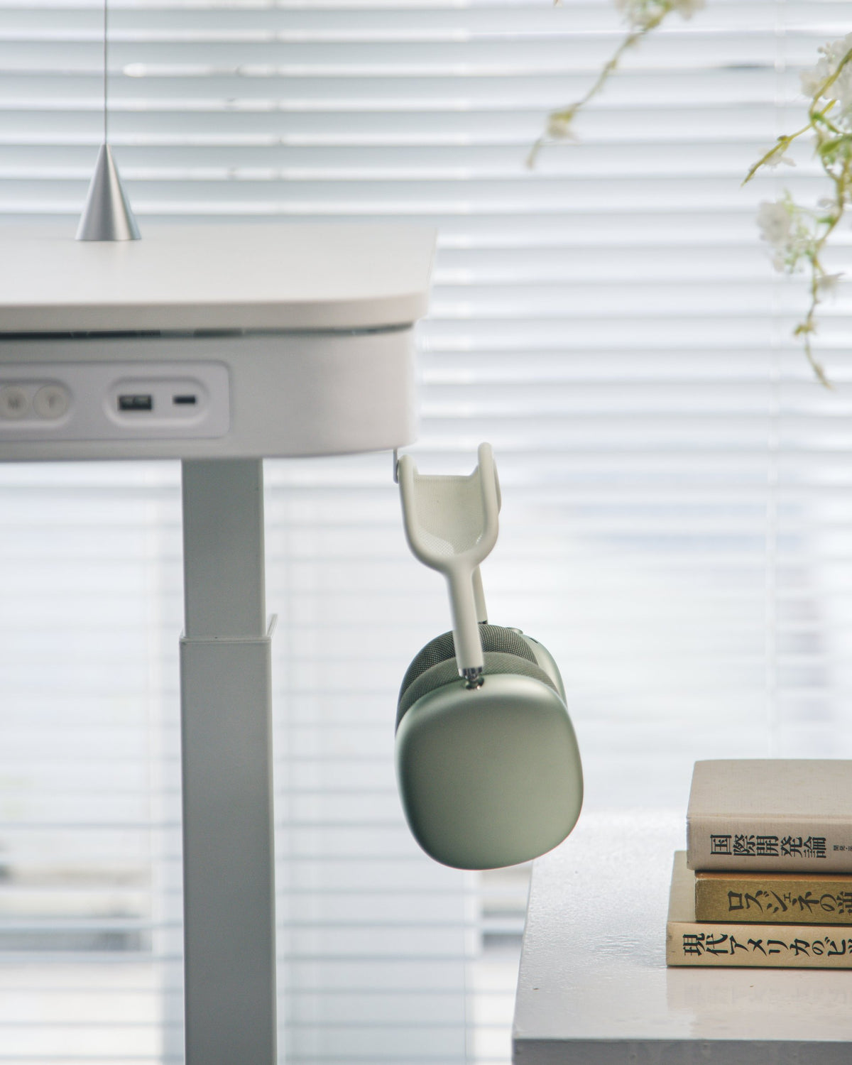 Green over-ear headphones hanging from an under-desk hook beside a stack of books
