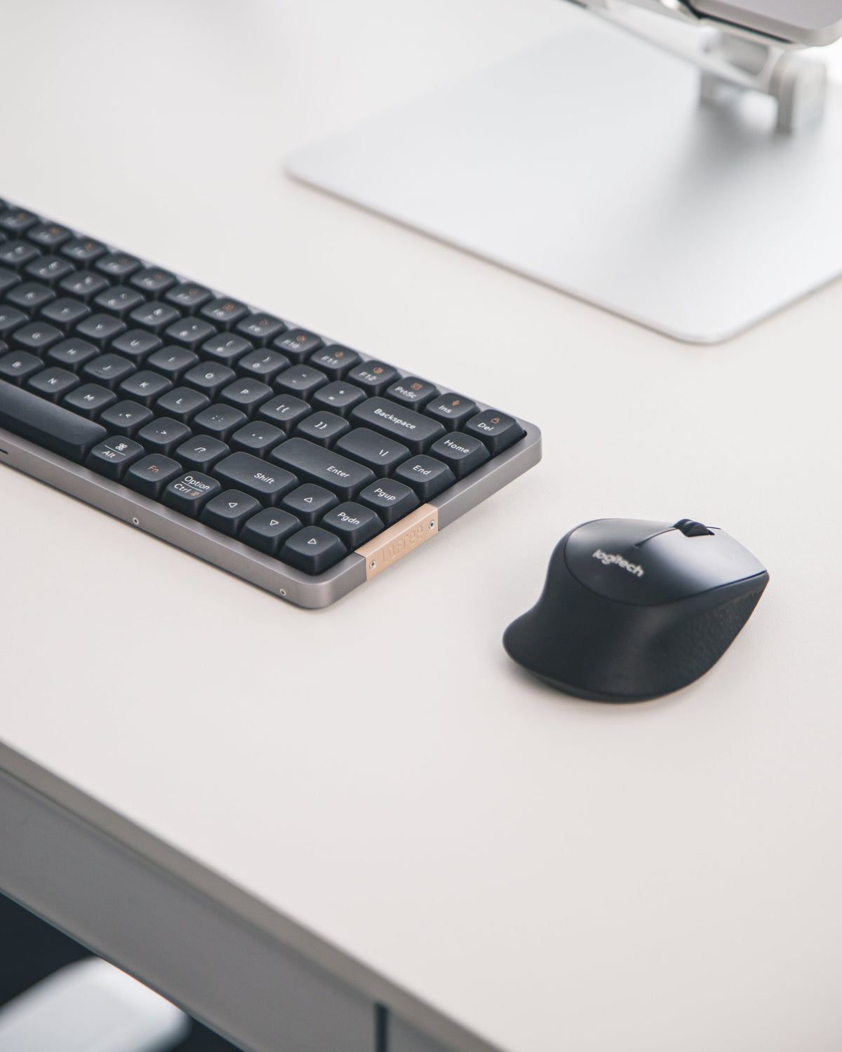 Low-profile wireless keyboard and mouse on a white desk under an aluminum laptop stand