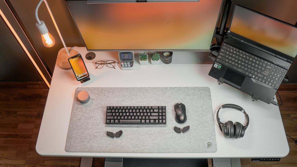 Top view of a white desk with a keyboard, mouse, headphones and laptop on an arm