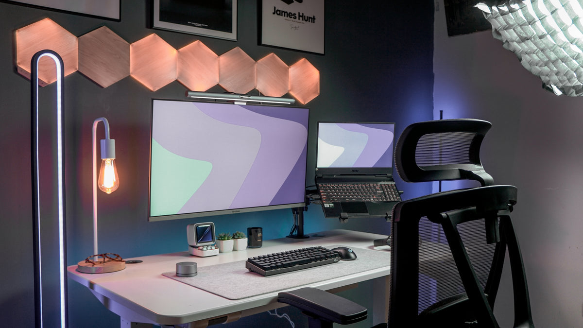 White desk setup with hexagon wall lights, floor lamp and laptop on a monitor arm