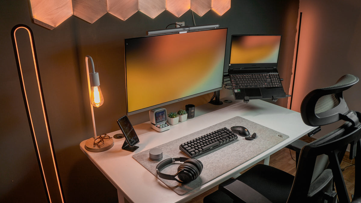 White desk with an amber wallpaper monitor, Edison lamp and headphones on a felt mat