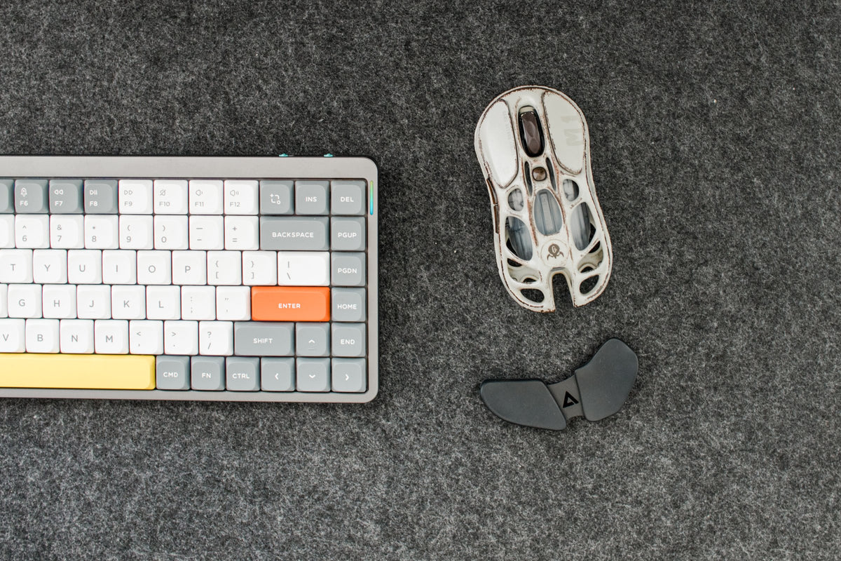 Gray and white mechanical keyboard with an orange enter key and a skeleton mouse on a dark felt desk mat