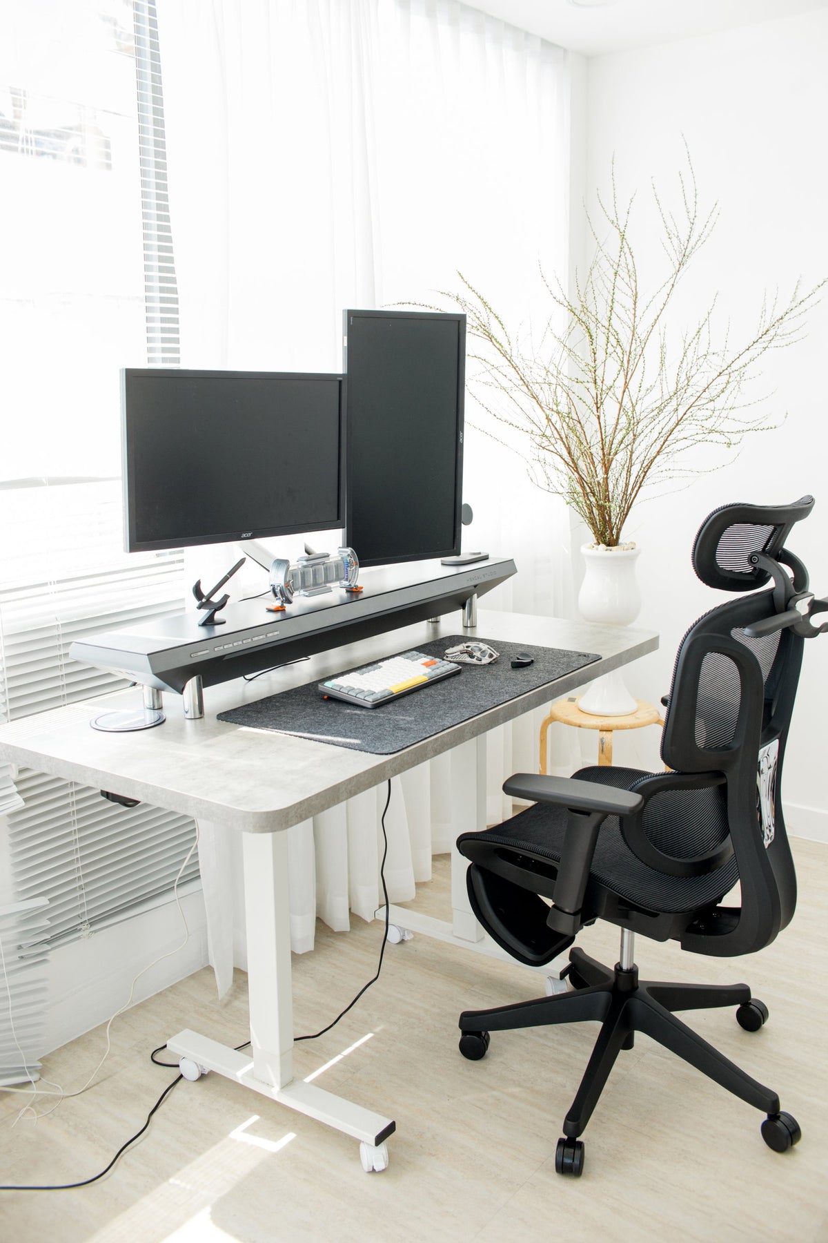 Bright white room with a dual-monitor standing desk and black ergonomic chair