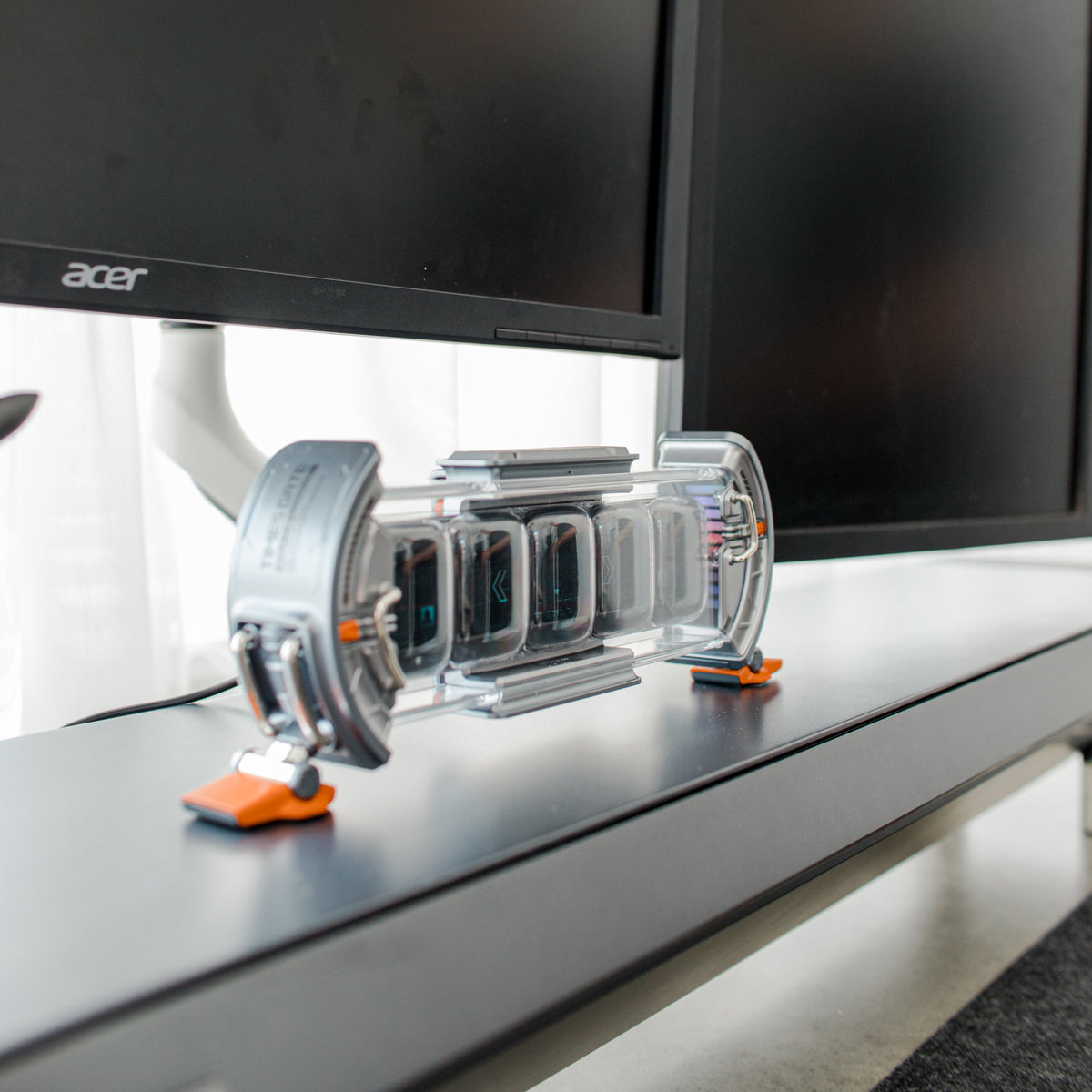 Transparent desk gadget on a black monitor shelf under two monitors