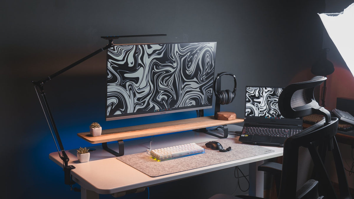 Dark desk with a wood monitor shelf, black and white marble wallpaper and an ergonomic chair